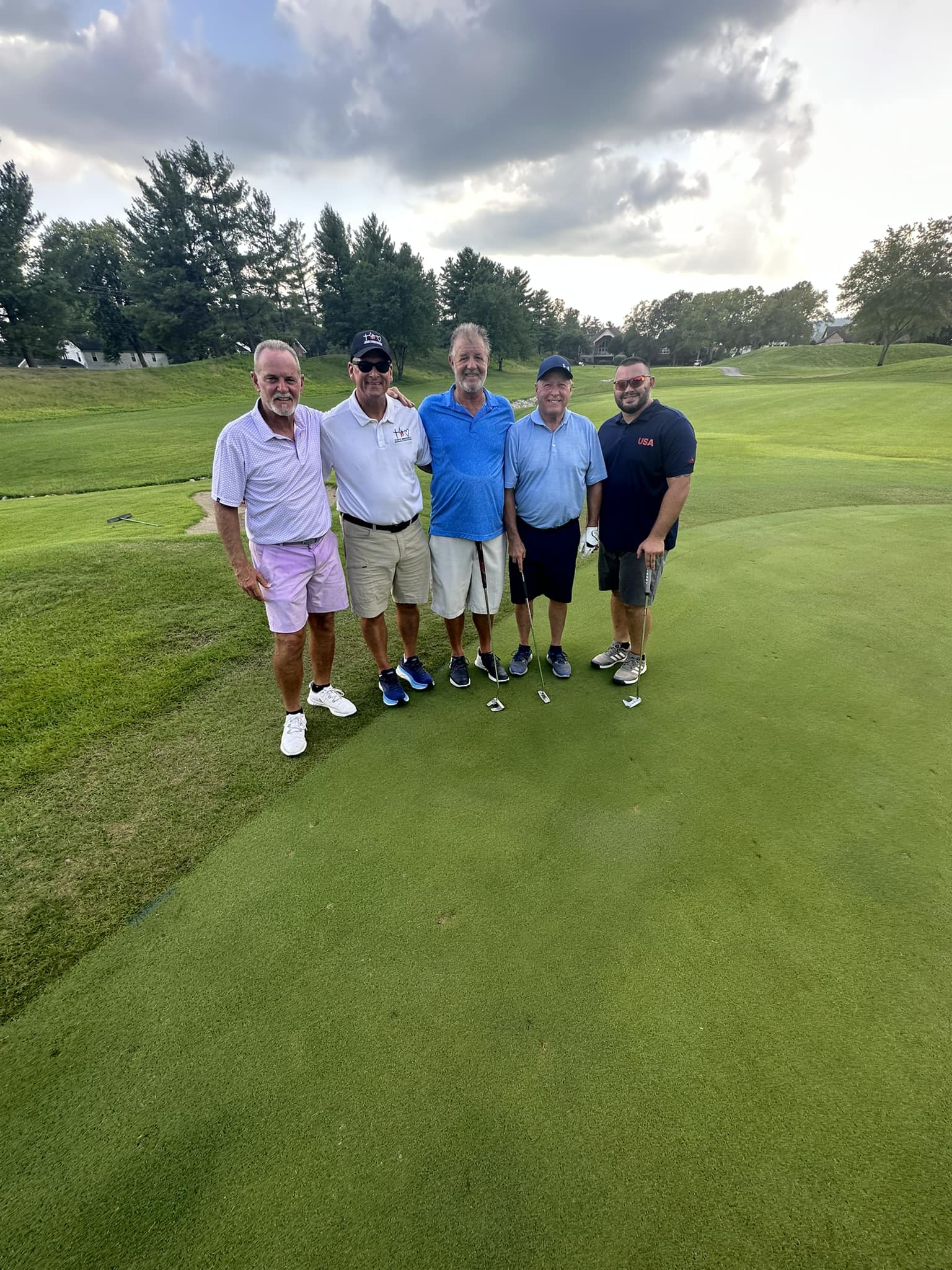 A group of golfers smiling together and holding their clubs.