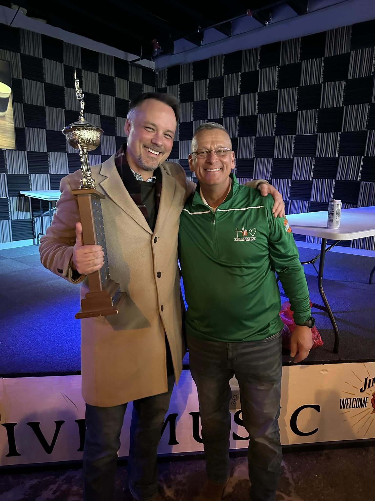 Two men posing for a picture with one of them holding a trophy